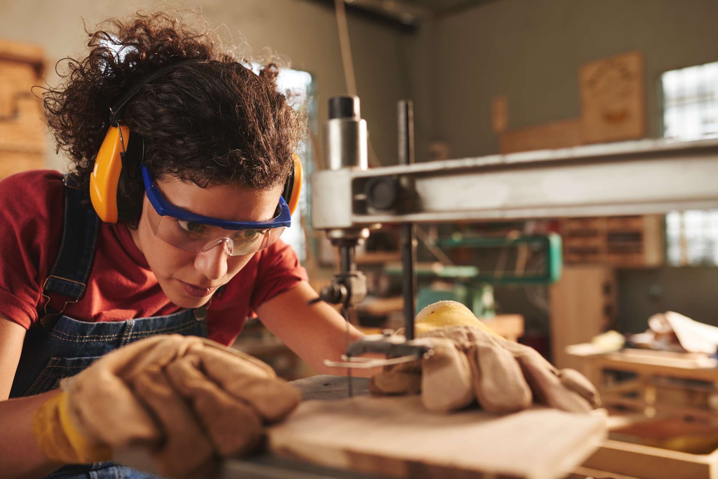 Carpenter wearing safety classes and hearing protection while drilling a whole in a wooden plank