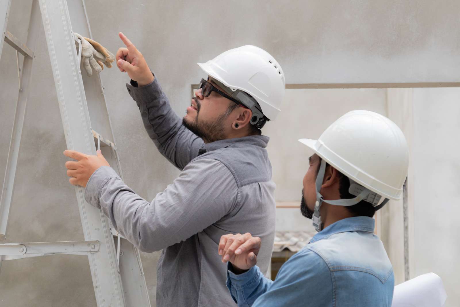 Two people on a worksite look up at the top of a ladder